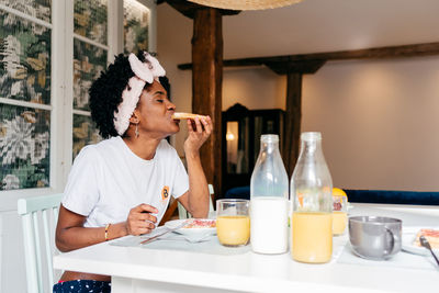 African american woman eating toast with jam while sitting at table and having breakfast at home