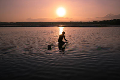 Silhouette man in sea against sky during sunset