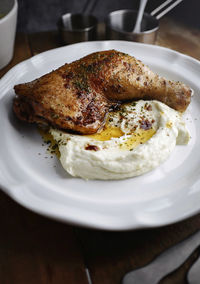 Roasted chicken and mashed cauliflower served on white plate on wood table.