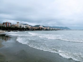 View of sea and buildings against cloudy sky