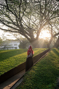 Rear view of mature woman wearing hijab standing on footpath in park during sunset