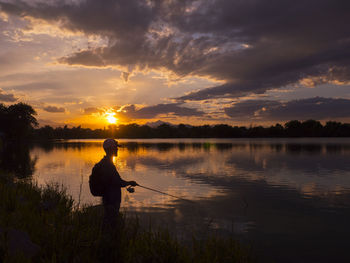 Silhouette man standing by lake against sky during sunset