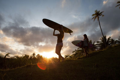 Two women carrying surfboards on a hill during sunset on siargao island, philippines