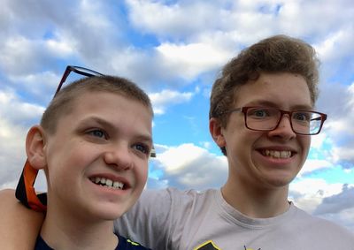 Head shot of two boys against a background of a bright blue sky and puffy white clouds