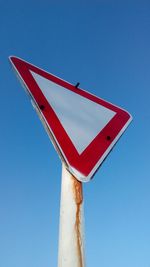 Low angle view of road sign against clear blue sky