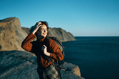 Man standing on rock by sea against clear sky