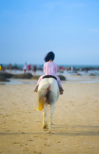 Rear view of woman riding horse on beach
