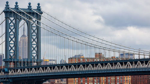 View of suspension bridge against cloudy sky and empire state building 