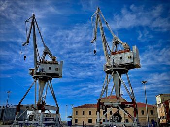 Low angle view of cranes at commercial dock against sky