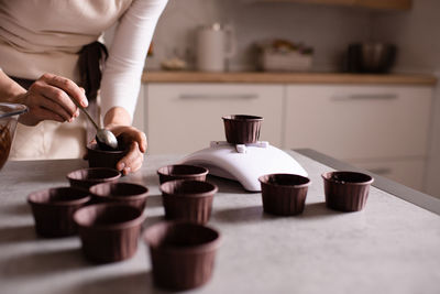 Woman making chocolate cupcakes weigh forms on kitchen scale on table close up.