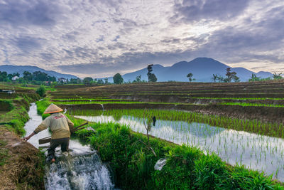 Rear view of people walking on mountain against cloudy sky