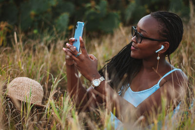 Young woman using mobile phone against grass and cactus trees 