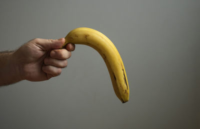 Cropped image of person holding banana against white background