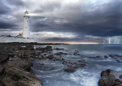 Lighthouse on sea by buildings against sky