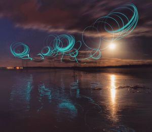 Light trails at beach against sky at night
