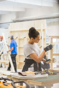 Young female trainee rubbing sand paper on wooden table at workbench