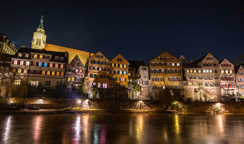 Illuminated buildings by river against sky at night