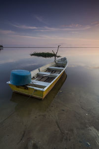 Boat moored on shore against sky during sunset