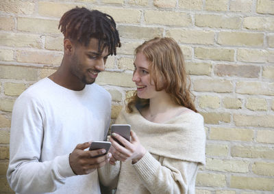 Young man using mobile phone against wall