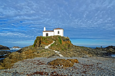 Lighthouse on cliff by sea against sky