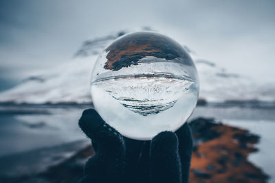 Cropped hand holding crystal ball with reflection by lake