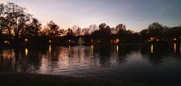 Silhouette trees by lake against sky at sunset