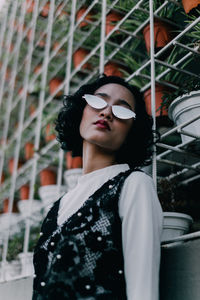 Portrait of woman wearing sunglasses standing against potted plants