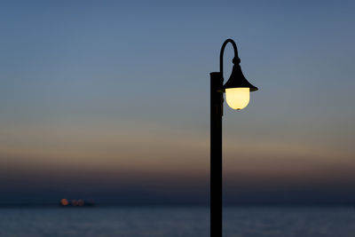 Street light by sea against sky during sunset