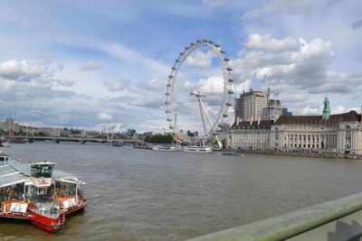 Ferris wheel in city against cloudy sky
