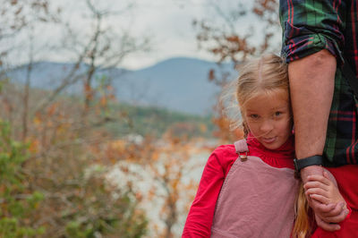 Little girl holds the hand of her father, standing with his back,  autumn forest landscape