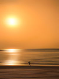 Silhouette man on sea against orange sky during sunset