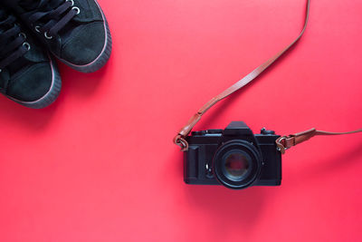 Directly above shot of black camera and shoes over pink background