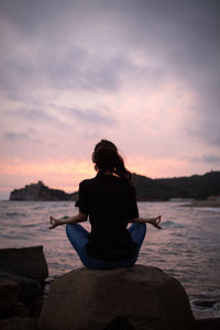 Rear view of woman doing yoga on rock at beach during sunrise