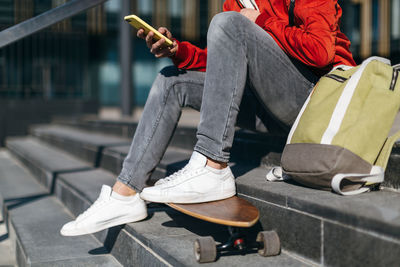 Trendy hipster with longboard sitting on the steps. man chatting by the mobile phone. 