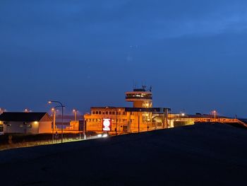 Illuminated buildings by street against sky at night