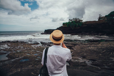 Rear view of man wearing hat standing at beach against sky