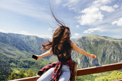 Woman with arms raised on mountain against sky