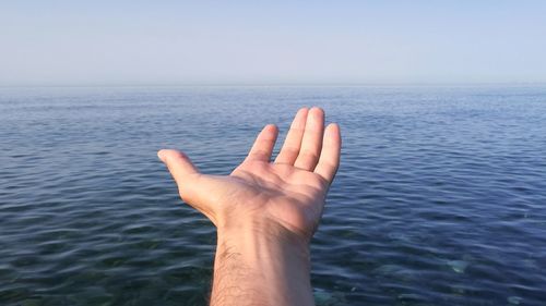 Cropped image of hand against sea