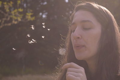 Close-up of beautiful woman blowing dandelion seed