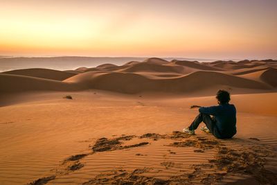 Man on sand dune in desert against sky during sunset