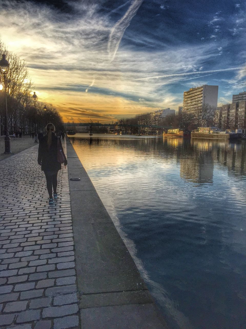 sky, built structure, architecture, water, building exterior, city, cloud - sky, lifestyles, sunset, walking, silhouette, city life, leisure activity, street, river, full length, person, cloud