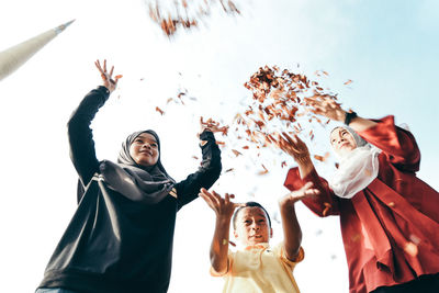 Low angle view of siblings playing with autumn leaves while standing against clear sky