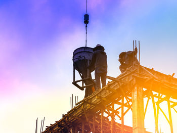 Low angle view of workers working on scaffolding against sky