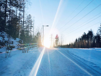 Road by snow covered trees against sky