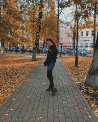 Portrait of young woman standing on footpath during autumn