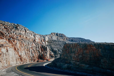 Road by rocky mountains against clear blue sky