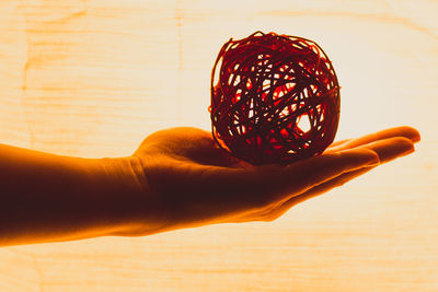 Cropped hand of person holding wicker ball against curtain