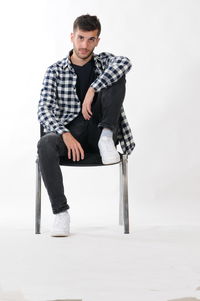 Full length portrait of young man sitting on chair over white background