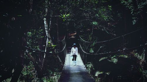 Rear view of woman walking on footpath amidst trees in forest