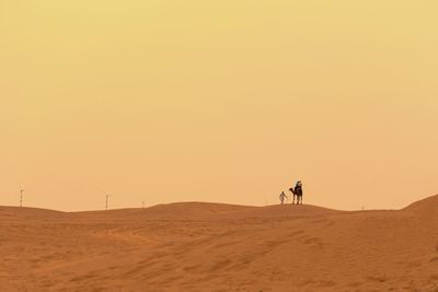 People riding in desert against sky during sunset
